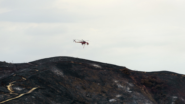 A firefighting helicopter flies over burned hills during the La Tuna fire in Los Angeles, California on Sunday.